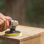 The carpenter uses a polishing machine to smooth the wood.