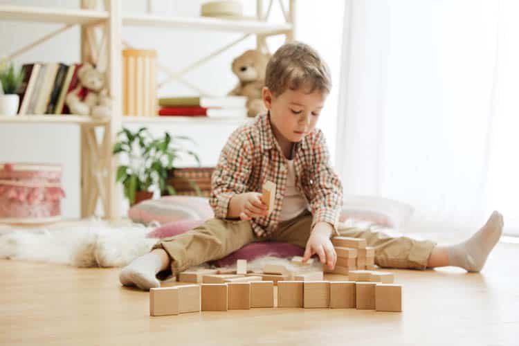 Little child sitting on the floor. Pretty boy palying with wooden cubes at home