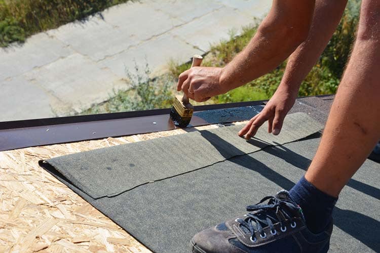 A building contractor is installing underlayment, a layer of bit