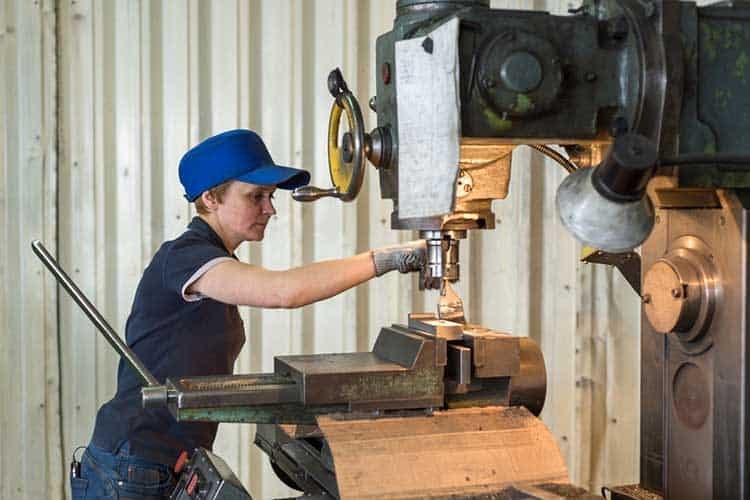 A woman at work on a vertical milling machine. Machining of a metal part on a metal-cutting machine.