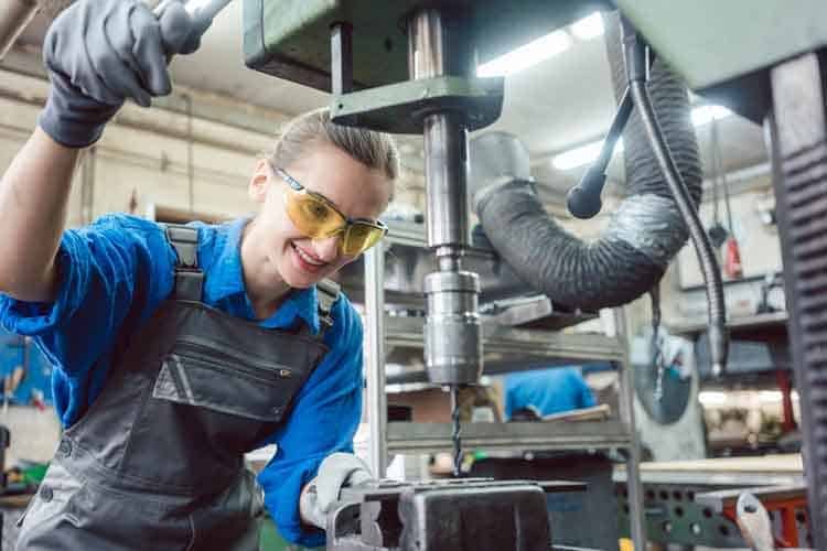 Woman worker in metal workshop using pedestal drill