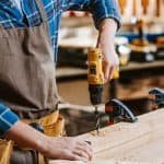Cropped view of carpenter in apron holding hammer drill